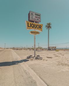 a large liquor sign in the middle of a dirt road with palm trees behind it