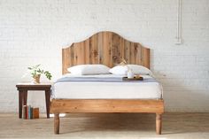 a bed with white pillows and wooden headboard in a room next to a table