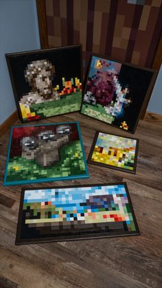 four pixel art pieces are displayed on a wooden table with two framed pictures in the background