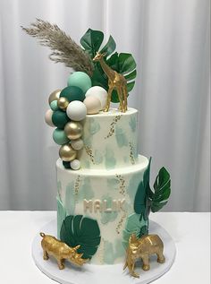 a three tiered cake decorated with green and gold decorations, including giraffes