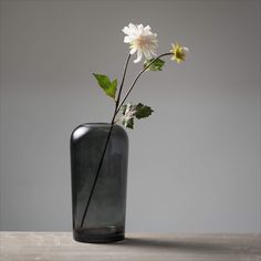 a black vase with white flowers in it sitting on a wooden table next to a gray wall