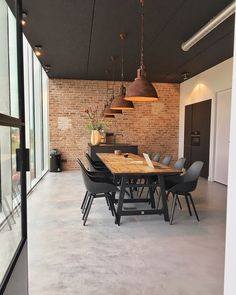 a dining room table with chairs and lights hanging from it's ceiling, in front of a brick wall