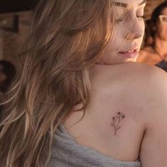 a woman with a small flower tattoo on her upper arm and shoulder, looking down at the ground