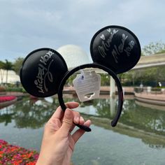 someone is holding up their mickey mouse ears in front of the water at disney world