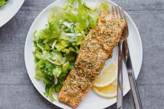 two white plates topped with fish and salad next to silverware on top of a table