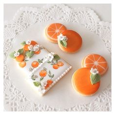 three decorated cookies sitting on top of a doily next to orange slices and flowers