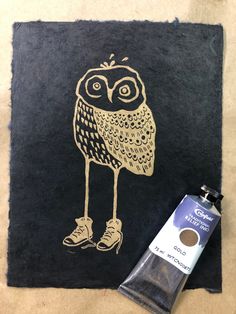 an owl painted on a black piece of paper next to a tube of glue