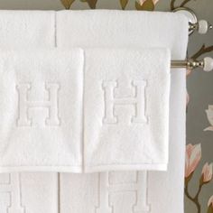 two white towels are hanging on the towel rack in front of a floral wallpaper