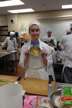 a woman holding a bowl with food in it while standing next to other people wearing chef hats and aprons