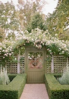 an outdoor garden with hedges and flowers on the top, along with a wooden gate