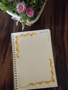 an open notebook sitting on top of a wooden table next to a potted plant