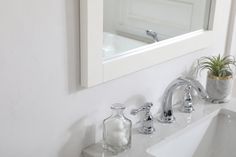 a bathroom sink with two faucets next to a mirror and a potted plant