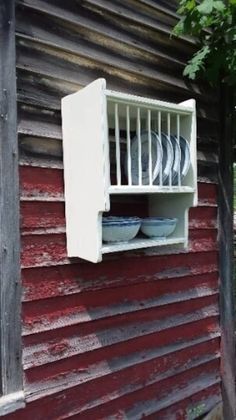 an old red house with plates and bowls on the window sill in front of it