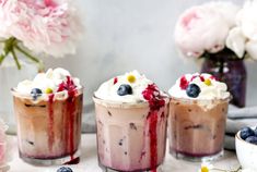 three desserts with blueberries and whipped cream in them on a table next to flowers