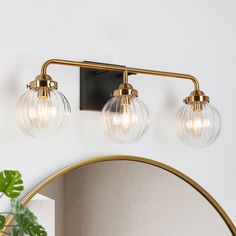 three light bathroom fixture with clear glass globes and brass finish on the wall next to a mirror