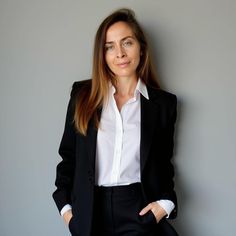 a woman wearing a black suit and white shirt standing in front of a gray wall