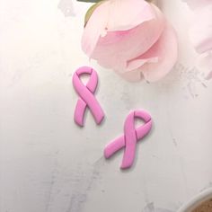 two pink ribbons are sitting next to a flower on a white table with flowers in the background