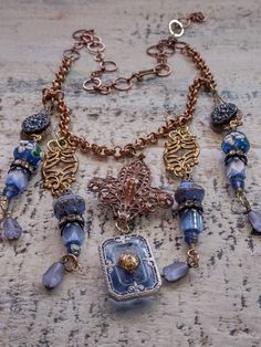 An assemblage of vintage components in a Bohemian style. The central assembled pendant is a vintage to antique fleur dis lis shape copper over brass component to which I've added a vintage German glass intaglio of the Eiffel Tower on the back. It suspends an Art Deco faceted blue glass cabochon in a filigree silver setting. Originally, this pendant would have had a rhinestone in the center, but it was missing, so I've added a gold plated brass filigree bead cap as a focal and to tie it in with the other brass elements in the design. Accompanying pendants are vintage Czech glass buttons, vintage Czech atlas glass and fire polished tulip shaped beads, Japanese 1930s glass beads and vintage lampwork beads with floral detail along with vintage caps and rhinestone rondelles. Length can be adjus Vintage Gold Necklaces With Patina, Vintage Metal Necklace With Patina, Vintage Patina Metal Necklace, Vintage Silver Copper Necklace, Vintage Copper Necklace In Silver, Vintage Silver Necklace With Copper, Handmade Antique Gold Necklaces For Vintage Collection, Handmade Antique Gold Necklace For Vintage Collection, Decorative Vintage Bronze Necklace