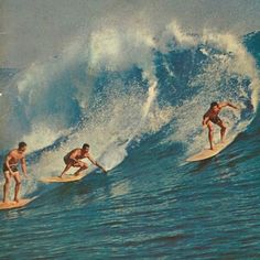 three men riding surfboards on top of a wave