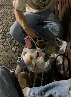 a man sitting on a bench with food and drinks in front of him, next to his feet