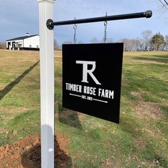 a sign hanging from the side of a white pole in front of a green field