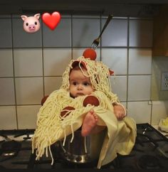 a baby sitting on top of a stove covered in spaghetti