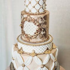 a three tiered cake decorated with gold and white decorations