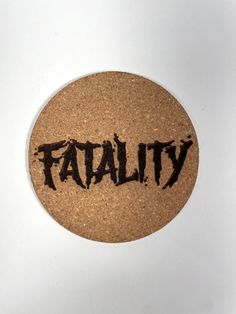 a cork coaster with the word fatal written in black ink on top of brown cork