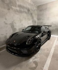 a black sports car parked in an empty parking space with concrete walls and flooring