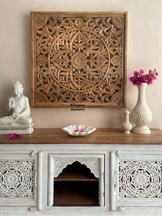 an ornate wooden carving on the wall above a white cabinet with vases and flowers