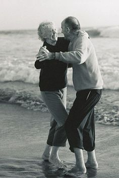 an older man and woman hugging on the beach