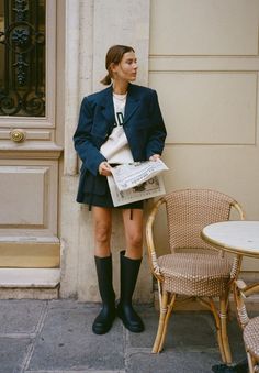 a woman standing in front of a door with her legs crossed and holding a newspaper