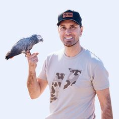 a man is holding a bird on his arm and smiling at the camera while wearing a baseball cap