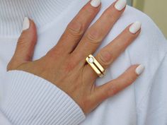 a woman's hand wearing a gold ring with a diamond on it and white nails