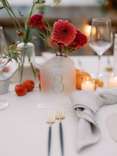 the table is set with silverware, napkins and red flowers in vases