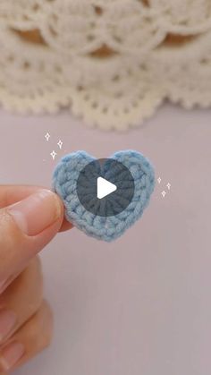 someone is holding a crocheted heart brooch with a video playing button on it