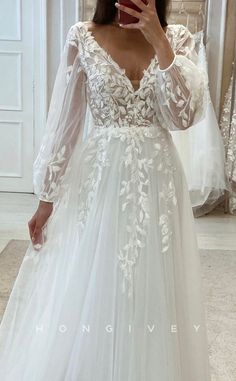 a woman taking a selfie wearing a wedding dress with long sleeves and floral appliques