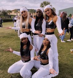 four women dressed in white pose for a photo together on the grass at an outdoor event