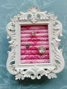 an ornate white frame with pink fabric in the middle and two rings on each side