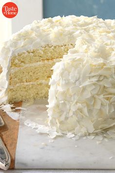 a cake with white frosting on a cutting board next to a knife and fork