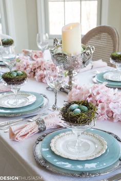 a table set for easter with blue and white plates, pink flowers and candlesticks