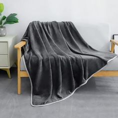 a gray blanket sitting on top of a wooden chair next to a white table and potted plant