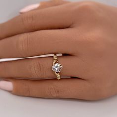 a woman's hand wearing a gold ring with a white diamond in the center