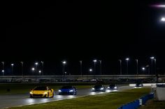 a group of cars driving down a race track at night with street lights in the background