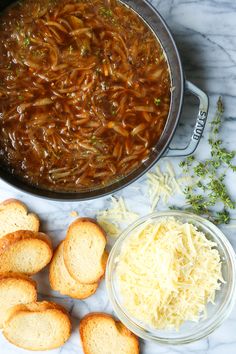 some bread and cheese are next to a pot of soup on a marble counter top