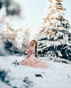 a woman in a pink dress is standing in the snow with her long hair pulled back