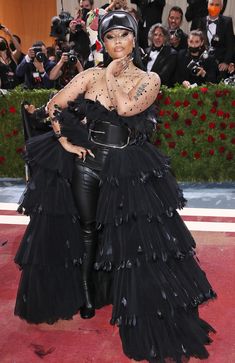 a woman in a black dress and headpiece standing on a red carpet with people taking pictures behind her