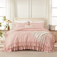 a bed with pink comforter and pillows in a white room next to a window