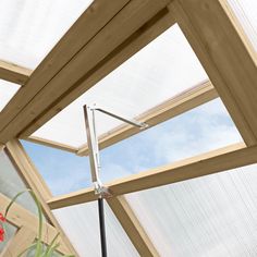 the inside of a glass house with a metal pole in it's center and red flowers on the other side