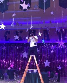 a man standing on a ladder in front of a stage with stars hanging from the ceiling